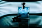 Artistic close-up of a blue perfume bottle with ambient lighting and water reflection.